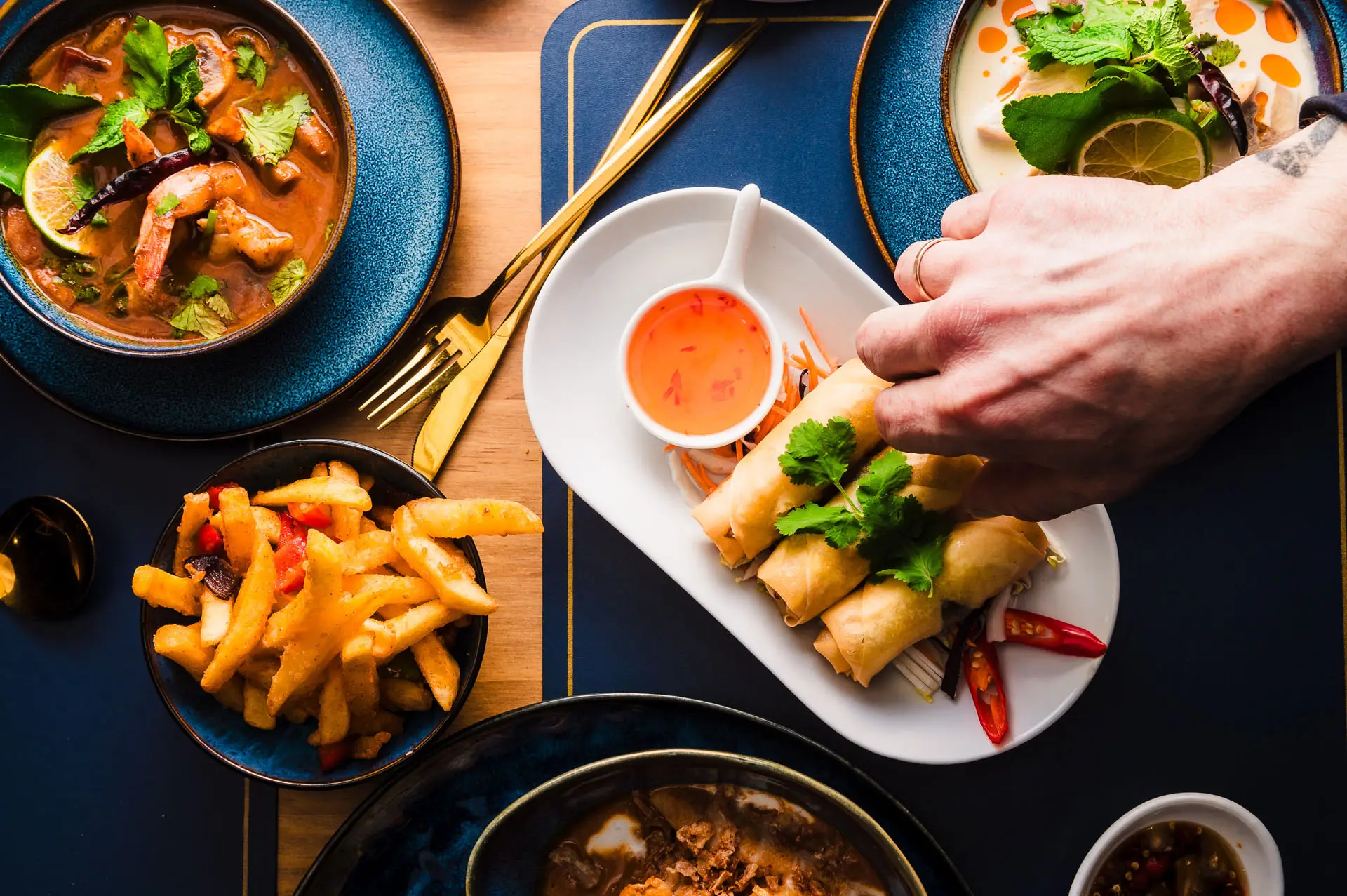 A table of Thai food: tom yum soup, spring rolls, salt and chilli fries